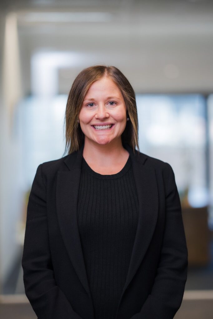 A women smiling facing the camera, dressed in a black blazer, posing for a headshot.