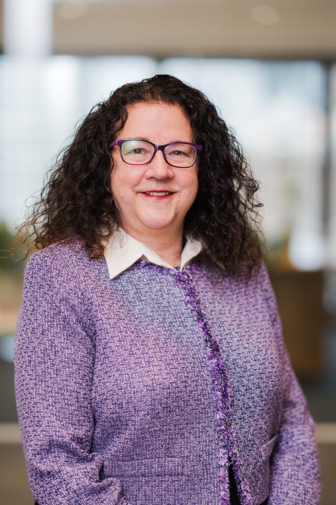 A women smiling, wearing a purple jacket, posing for a headshot.
