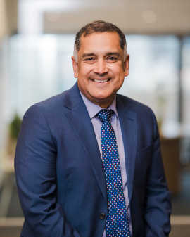 A man smiling, wearing a navy suit and tie, posing for a headshot.
