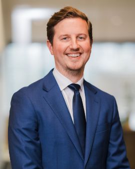 A man smiling, wearing a navy suit and tie, posing for a headshot.