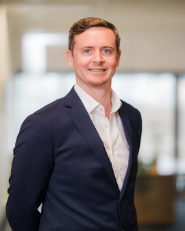 A man smiling, wearing a navy suit, posing for a headshot.