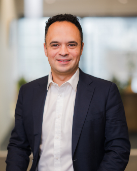A man smiling, wearing a navy suit, posing for a headshot.