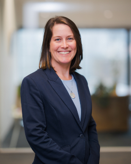 A woman smiling wearing a navy blazer, posing for a headshot.